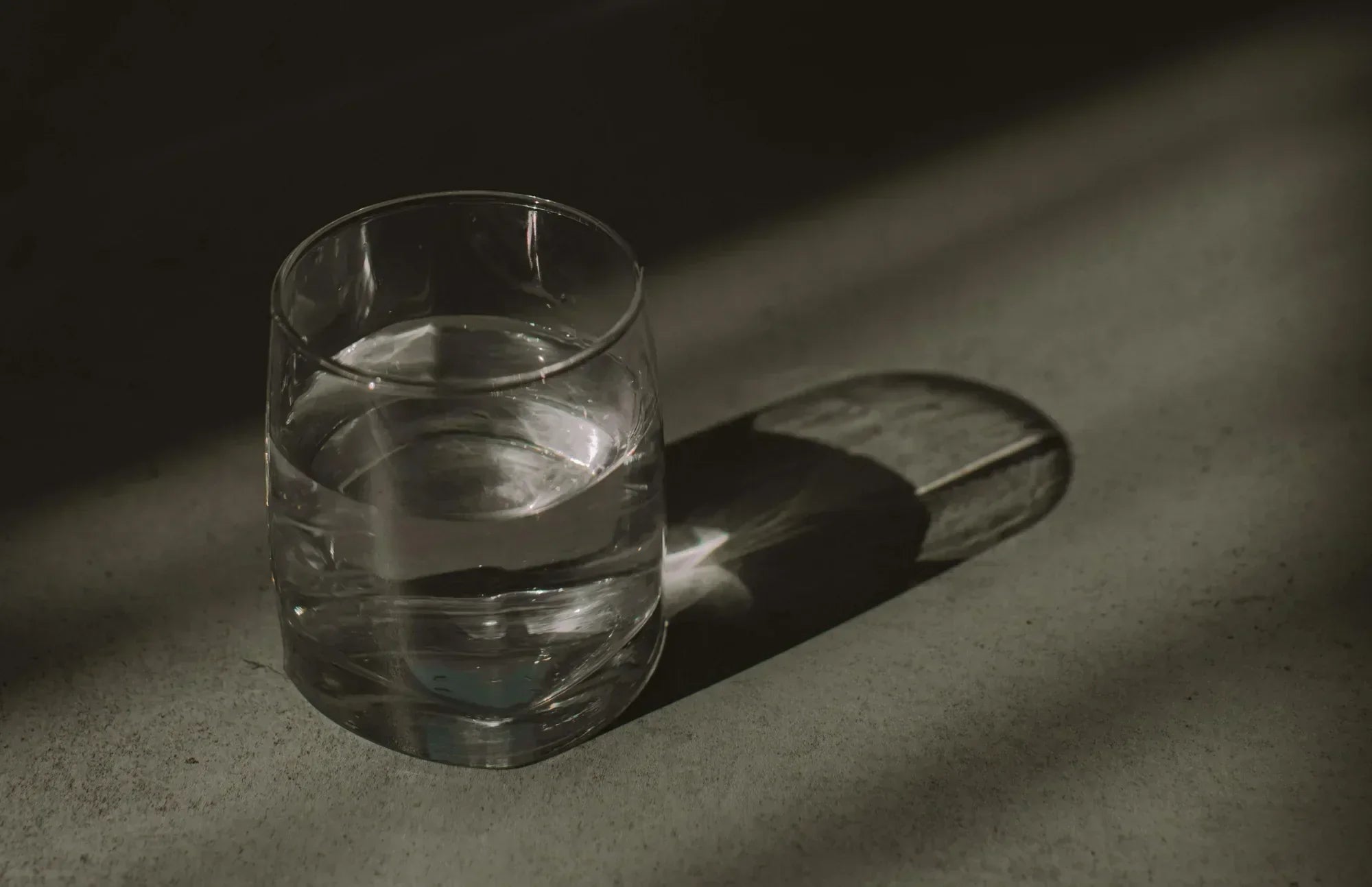 Clear glass of water casting a shadow in soft lighting—representing hydration and the simple daily act of taking a probiotic supplement with water.