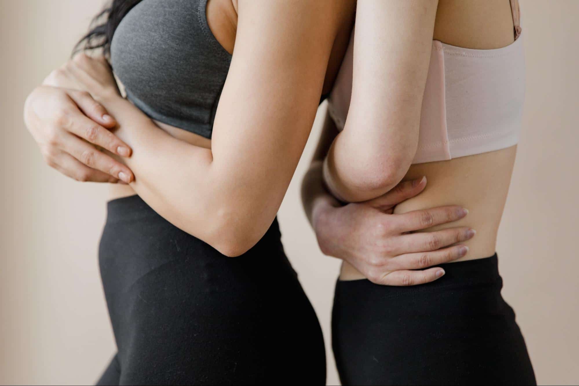 Two women standing back to front holding their stomachs
