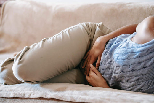 A constipated woman on a couch holding her stomach.