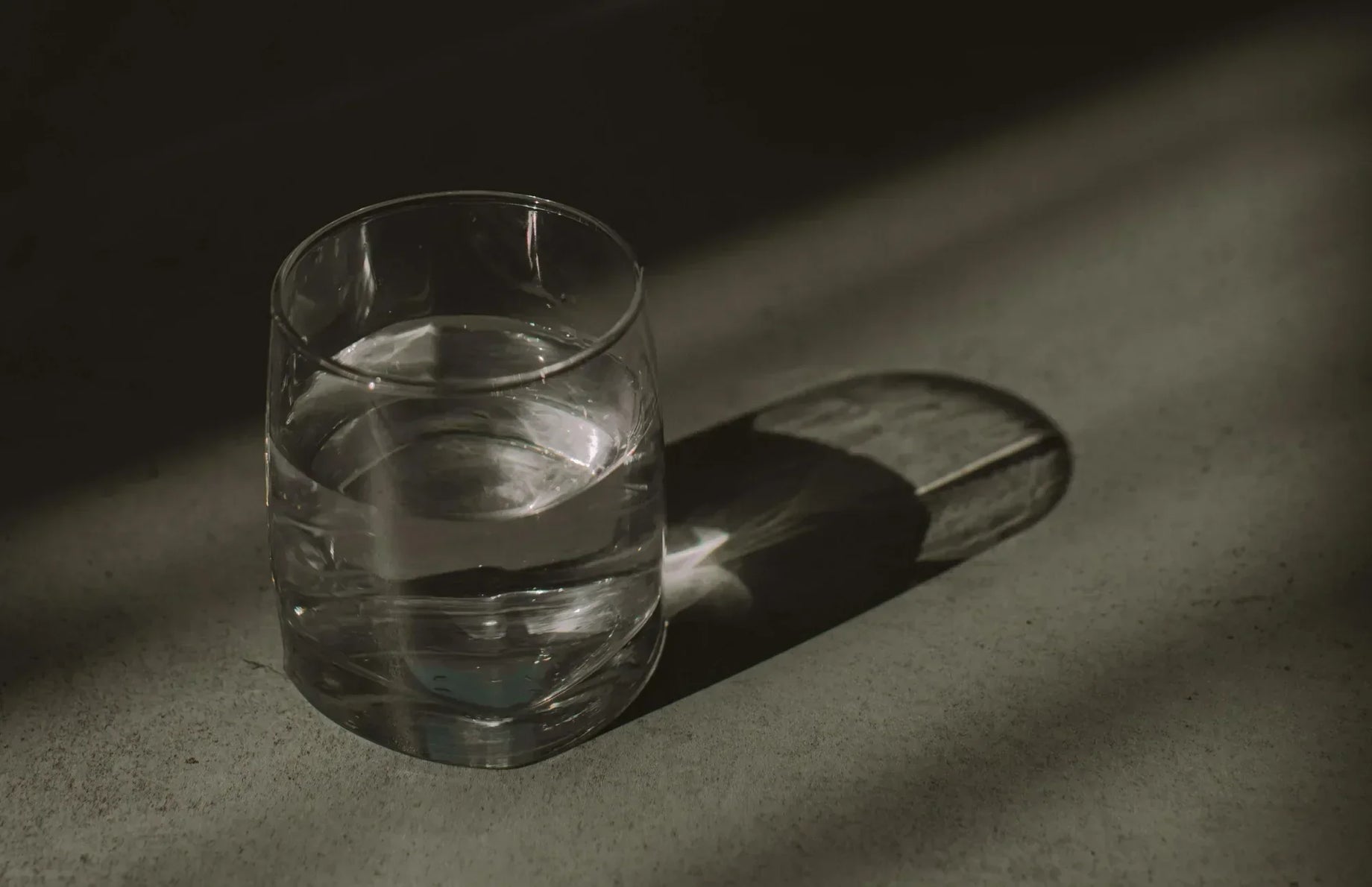 Clear glass of water casting a shadow in soft lighting—representing hydration and the simple daily act of taking a probiotic supplement with water.