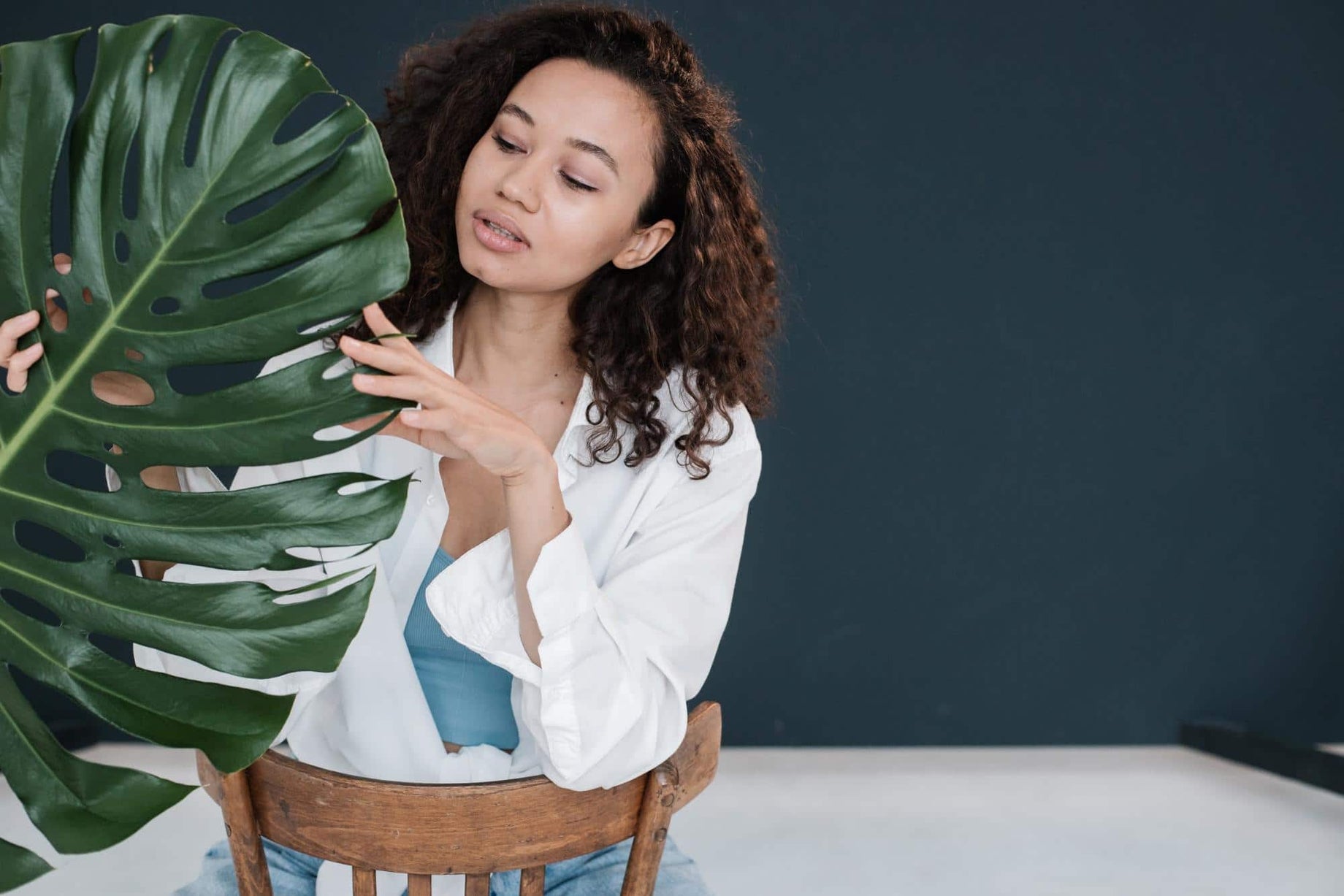 Photo of a healthy young woman sitting In a chair touching a plant. Taking prebiotics can help support the good bacteria in your gut and reinforce overall health.