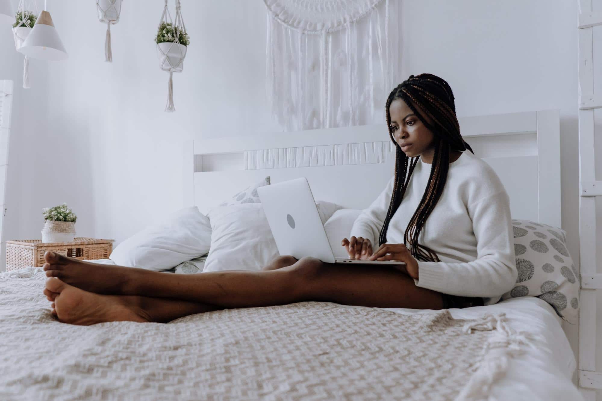 Healthy young woman sitting on her bed using a laptop to research the difference between prebiotics and probiotics.