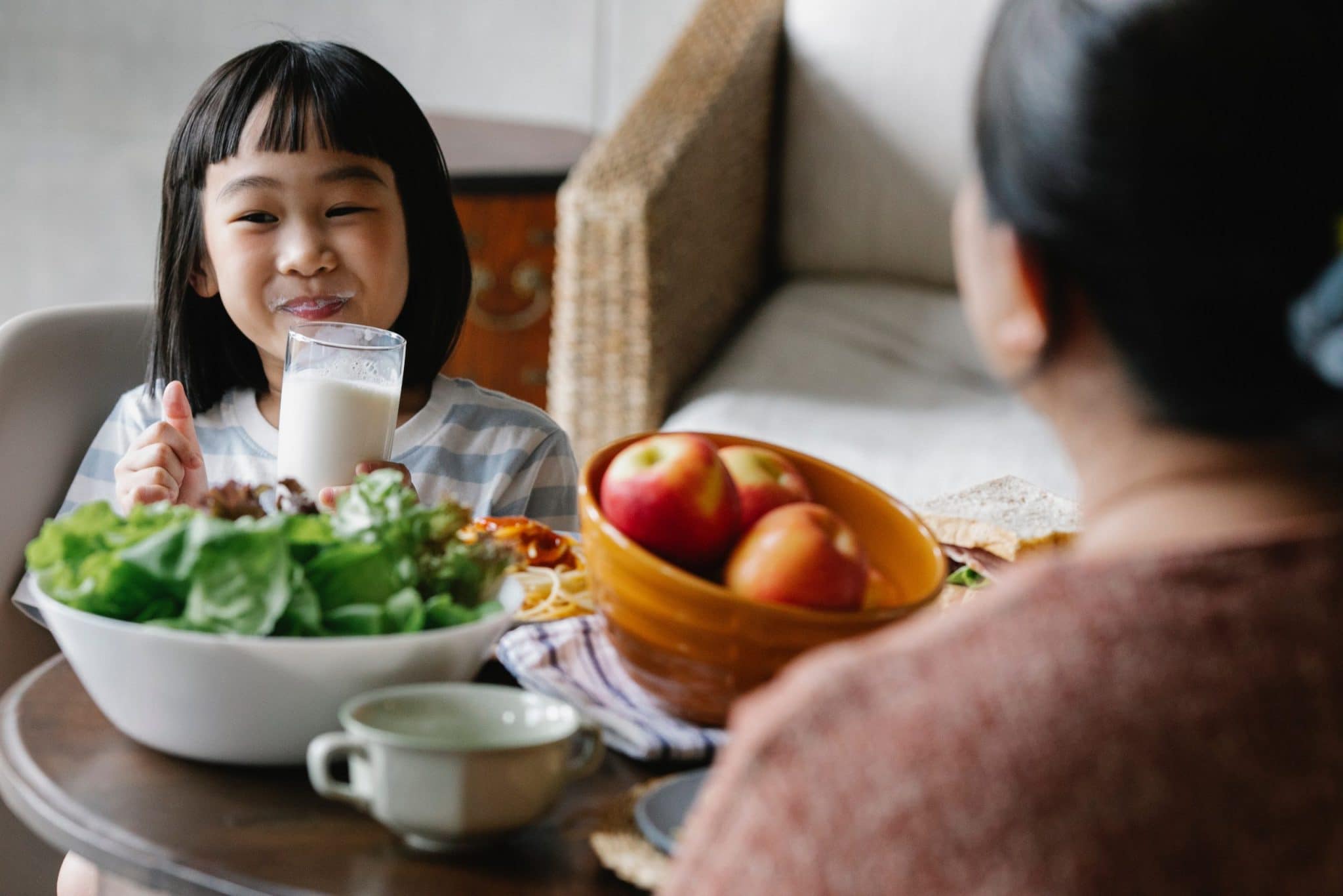 A happy child and her mother eat a meal together with a good mix of probiotic and prebiotic foods including apples and leafy greens.