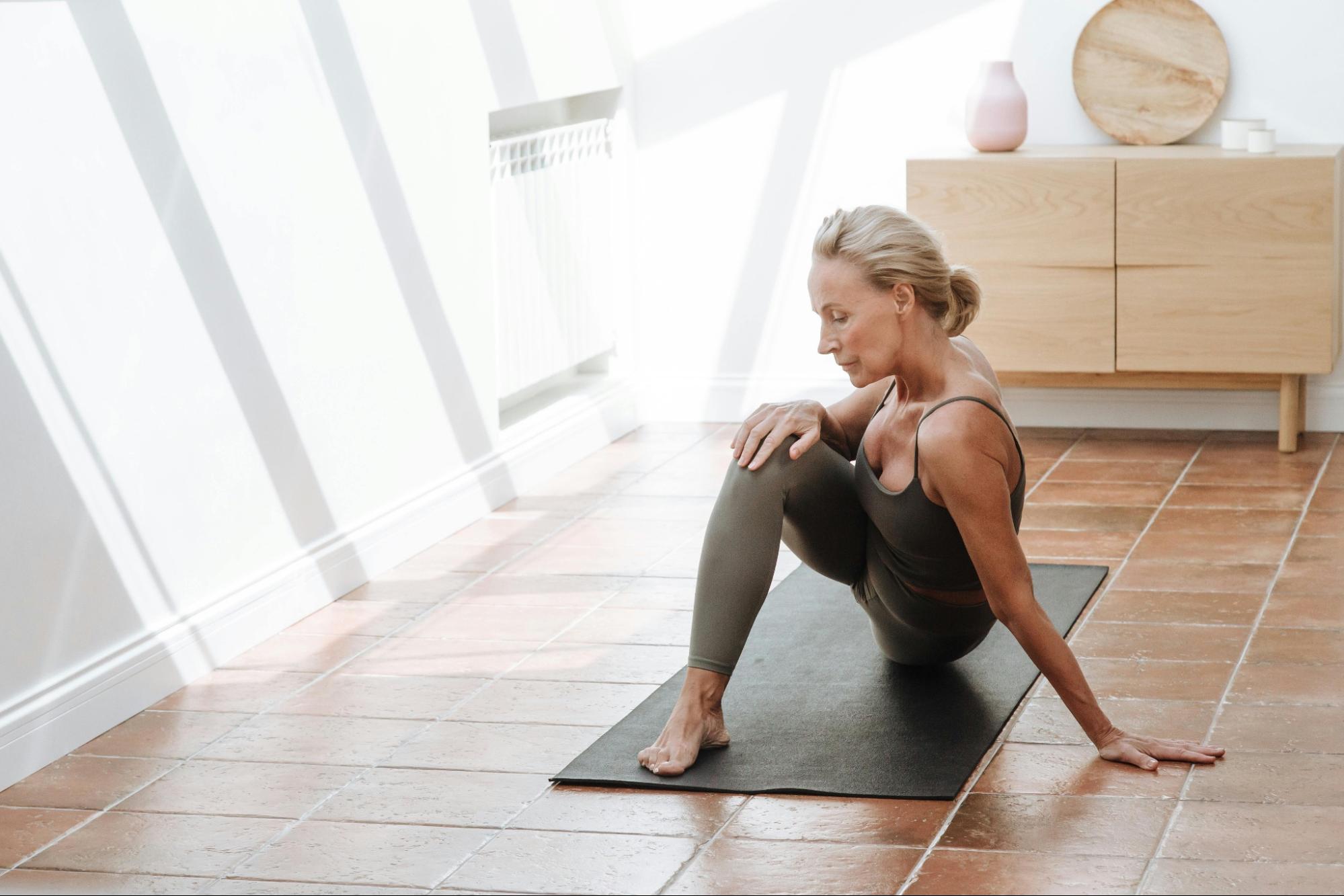 Woman practicing yoga on a mat in a bright room with wooden flooring and white walls.