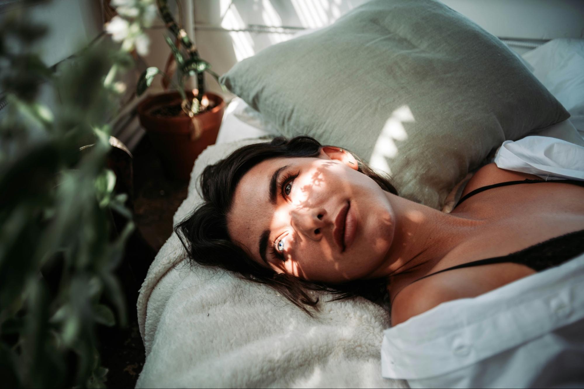 Woman lying on a bed with sunlight filtering through, surrounded by plants.